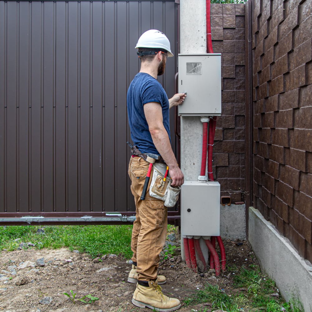 Professional technician installing automatic sliding gate motor and control system with tools and equipment